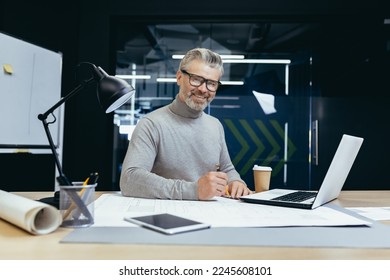 Portrait of senior architect, gray haired designer smiling and looking at camera, man mock up plan use laptop and tablet computer at work inside studio office. - Powered by Shutterstock