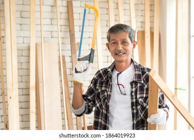 Portrait Senior Asian Elderly Old Man Carpenter Wearing White Gloves Protection Holding Hand Saw With Smile And Happy Emotion In Workshop