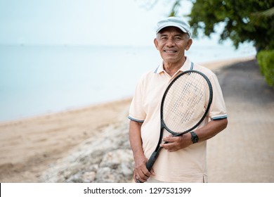 portrait of senior asian man smiling with racket tennis in hand