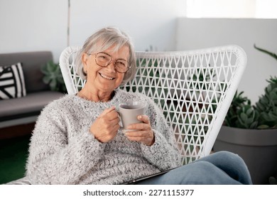 Portrait of senior attractive woman with cheerful smile relaxing at the armchair in the balcony at home looking at camera holding a coffee cup - Powered by Shutterstock