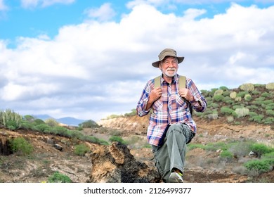 Portrait of a senior bearded man carrying a backpack looking at the mountain and smiling. Fit old man on a hiking trip enjoying adventure freedom and healthy vacation - Powered by Shutterstock
