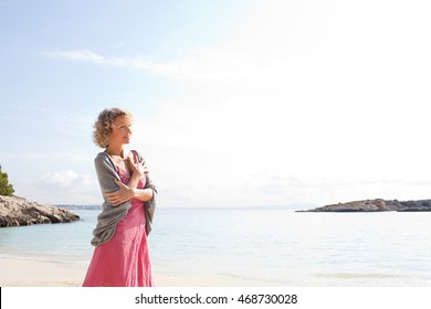 Portrait of a senior beautiful woman on beach destination shore smiling joyful looking ahead contemplating clear blue sea, aspirational travel lifestyle, outdoors nature.