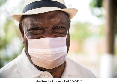 Portrait Of Senior Brazilian Black Man With Mask And White Hat Looking At Camera Spot In Sunset And Smiling. Horizontal Shape, Copy Space.