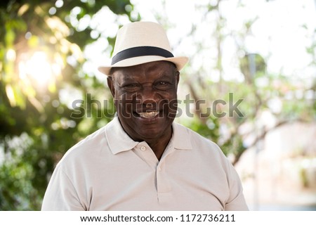 portrait of senior brazilian black man with white hat looking at camera spot in sunset and smiling. Horizontal shape, copy space.