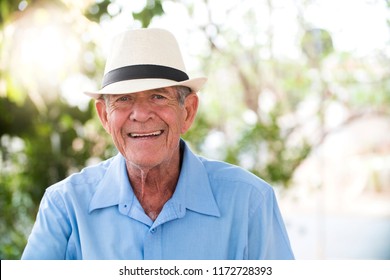 portrait of senior brazilian man with white hat looking at camera against green wall and smiling. Horizontal shape, copy space