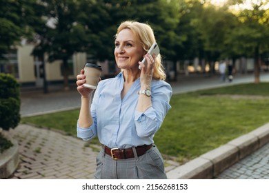 Portrait Of Senior Business Woman Hold The Paper Cup And Talking Phone In The City. Happy Mature Business Woman 50s