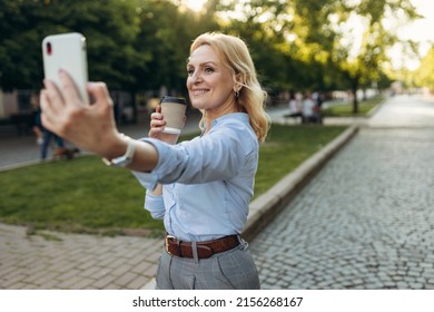 Portrait Of Senior Business Woman Hold The Paper Cup And Take Selfie In The City. Happy Mature Business Woman 50s