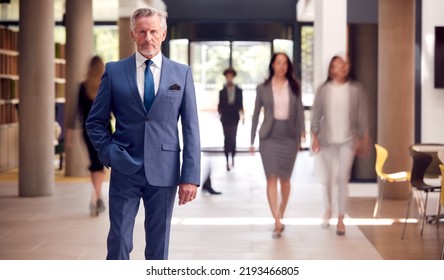 Portrait Of Senior Businessman CEO Chairman Standing In Lobby Of Busy Modern Office Building