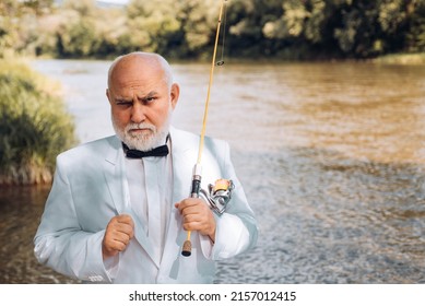 Portrait of senior businessman fishing. Excited mature man fisherman in suit with fishing rod, spinning reel on river.