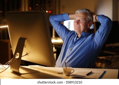 Portrait Of Senior Businessman Sitting In Front Of Computer And Leaning Back While Satisfied To Solve The Problem. Professional Man Working Late Night. 