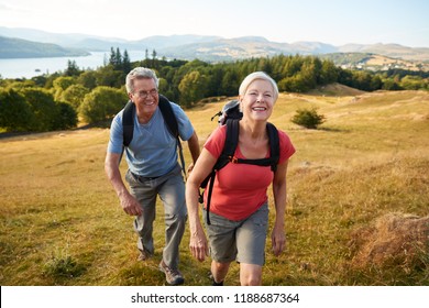 Portrait Of Senior Couple Climbing Hill On Hike Through Countryside In Lake District UK Together