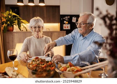 Portrait of senior couple at dining table at cozy apartment having healthy lunch. Senior man serving food on plate. - Powered by Shutterstock