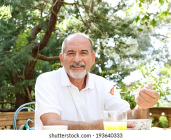 Portrait Of A Senior Couple Enjoying A Healthy Breakfast Together In A Luxury Home Garden On Holiday. Mature People Eating Healthy Food And Enjoying Each Others Company, Outdoors. Travel Lifestyle.