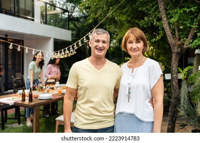 Portrait Of Senior Couple Looking At Camera While Having Party Outdoor. Attractive Mature Older Parents Having Dinner, Eating Foods, Celebrate Weekend Reunion Gathered Together At Dining Table At Home