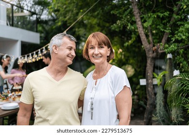 Portrait of senior couple looking at camera while having party outdoor. Attractive mature older parents having dinner, eating foods, celebrate weekend reunion gathered together at dining table at home - Powered by Shutterstock