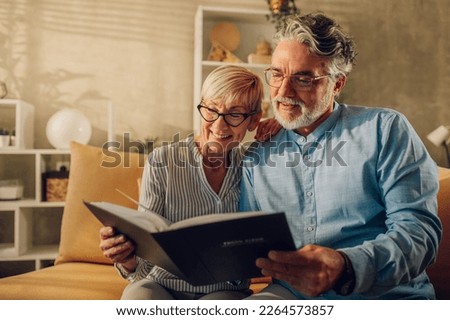 Portrait of a senior couple looking into their photo album while sitting on a couch at home. Mature spouses talking of marriage history and raising their children trough the years.