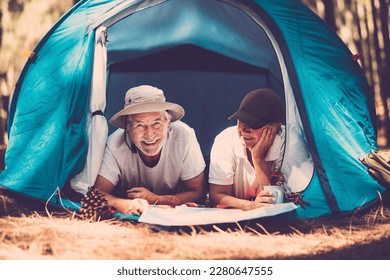 Portrait of senior couple relaxing inside a tent in free camping woods alternative travel vacation lifestyle. Old mature man and woman enjoy together freedom and retirement lifestyle outdoor leisure - Powered by Shutterstock