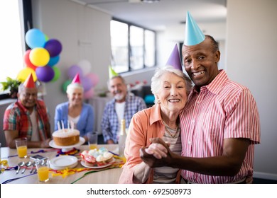 Portrait of senior couple standing by table during birthday party with friends in background