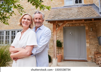 Portrait Of Senior Couple Standing Outside Front Door Of Home