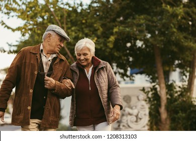 Portrait Of Senior Couple Talking And Walking Outdoors On Winter Day. Elderly Man Holding Hand Of His Female Partner And Walking On Street.