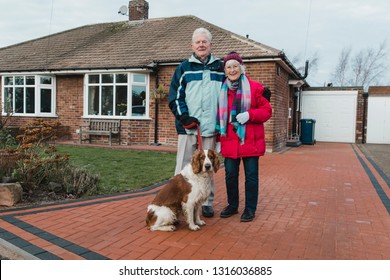 Portrait Of A Senior Couple And Their Pet Dog In The Front Yard Of Their House.