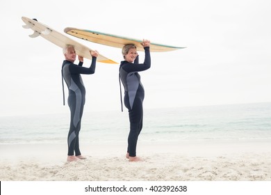 Portrait of senior couple in wetsuit carrying surfboard over head on the beach - Powered by Shutterstock