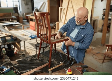 Portrait of senior craftsman repairing old furniture in carpentry workshop, copy space - Powered by Shutterstock