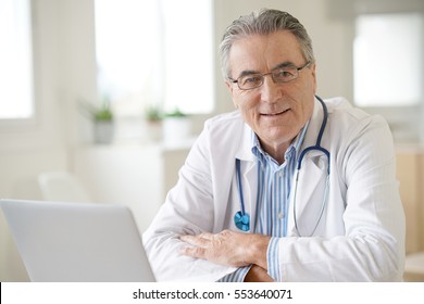 Portrait Of Senior Doctor Sitting In Medical Office