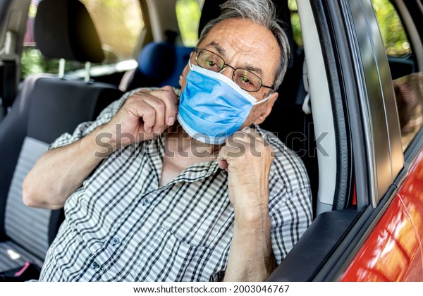Portrait of senior driver wearing protective medical\
mask. Old man with facial mask due to coronavirus ready to drive\
his car. New normal life until the end of the pandemic. Man driving\
with face mask