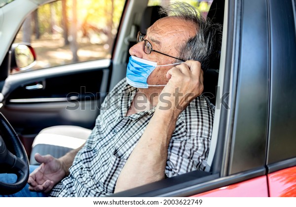 Portrait of senior driver wearing protective medical\
mask. Old man with facial mask due to coronavirus ready to drive\
his car. New normal life until the end of the pandemic. Man driving\
with face mask