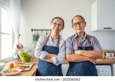 Portrait Of Senior Elderly Couple Wear Apron Smiling, Look At Camera. Attractive Strong Older Man And Woman Grandparent Wear Eyeglass Stand In Kitchen Enjoy Retirement Activity At Home. Family Concept