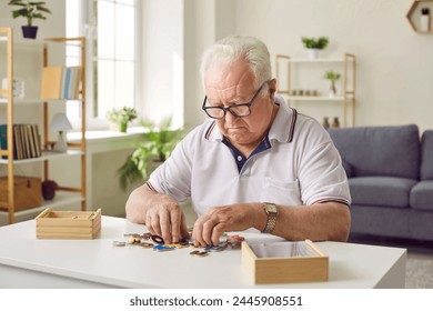 Portrait of a senior elderly sad gray-haired man collecting wooden jigsaw puzzles game at home sitting at the table. Memory training for dementia prevention and retirement leisure concept. - Powered by Shutterstock