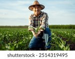 Portrait of senior farmer in corn field looking at camera holding crop in hands at sunset.