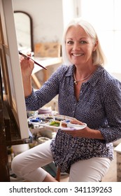 Portrait Of Senior Female Artist Working On Painting In Studio