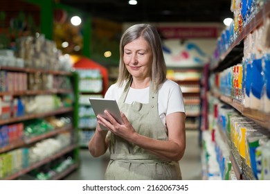 Portrait Of Senior Female Consultant, Employee In Grocery Store, Supermarket. Stands With A Tablet, Accepts The Goods, Checks. In Work Clothes.