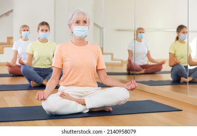 Portrait Of Senior Female In Face Mask Making Yoga Meditation In Lotus Pose In Fitness Studio