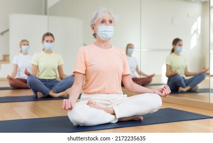 Portrait Of Senior Female In Face Mask Making Yoga Meditation In Lotus Pose In Fitness Studio