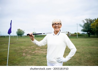 Portrait Of Senior Female Golfer With Golf Club Standing On Golf Course.