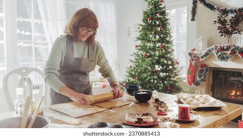 Portrait of Senior Female Preparing Dough for Making Gingerbread for Christmas at Home. Cheerful Housewife and Grandmother Making Pastries to Share with Family and Friends for the Holiday - Powered by Shutterstock