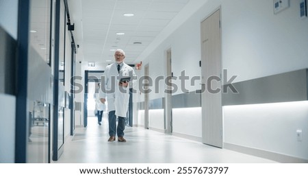 Portrait of a Senior General Practitioner Using Tablet Computer to as He is Walking and Browsing Patient's Medical History. Hospital Personnel Walking Through a Modern Clinic Corridor