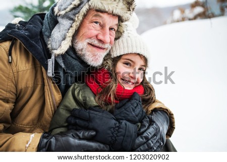 A portrait of senior grandfather and a small girl in snow on a winter day.