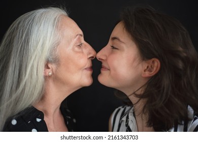 Portrait Of Senior Grandmother With Her Granddaughter Looking At Each Other Face To Face, Over Black Blackground