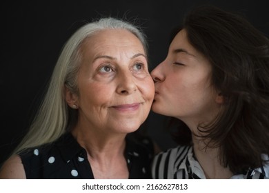 Portrait Of Senior Grandmother With Her Granddaughter Kissing Her Over Black Blackground