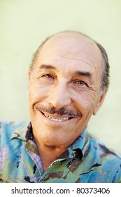 Portrait Of Senior Hispanic Man Looking At Camera Against Green Wall And Smiling. Horizontal Shape, Copy Space