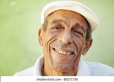 Portrait Of Senior Hispanic Man With White Hat Looking At Camera Against Green Wall And Smiling. Horizontal Shape, Copy Space