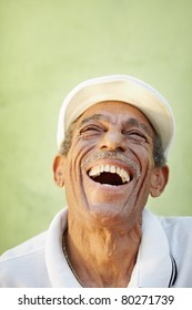 Portrait Of Senior Hispanic Man With White Hat Looking Up Against Green Wall And Smiling. Vertical Shape, Copy Space