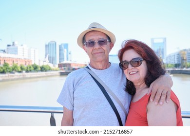 Portrait Of A Senior Hispanic Tourist Couple In Puerto Madero, A Trendy Neighborhood In Buenos Aires, Argentina. Concepts: Traveling And Enjoying The Outdoors, Active Retirement.