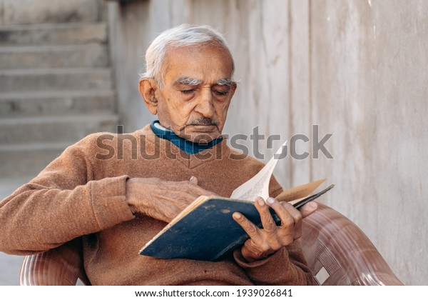 Portrait of Senior\
Indian man turning pages while reading book at home during corona\
virus pandemic 2021. Retired, Old people lifestyle. Old people\
hobby, leisure\
activity