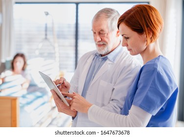 Portrait of senior male doctor standing in hospital room, talking to a nurse. - Powered by Shutterstock