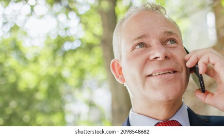 Portrait Of Senior Male Executive On His Phone Outdoors With A Positive Expression On His Face